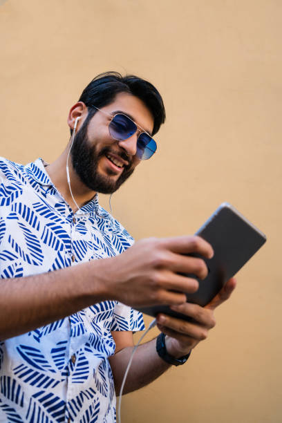 istock Latin man using his digital tablet with earphones. 1263646391