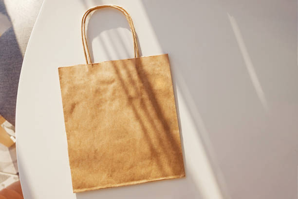 Craft paper bag mock-up on the white table with hard shadows.