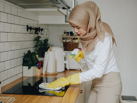Young muslim woman cleaning modern cooking glass ceramic electric surface with sponge and detergent