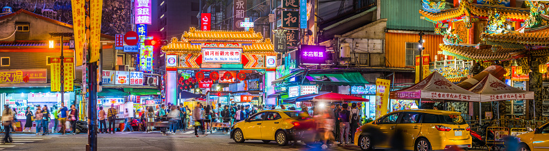 The crowded pavements of Raohe Street Night Market  beside the ornate facade of Songshan Ciyou Temple in the heart of Taipei, Taiwan’s vibrant capital city.