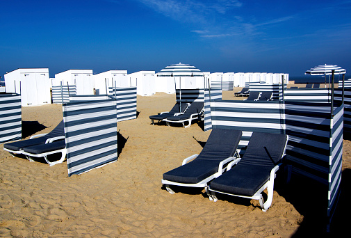 Sand Beach with Striped Sun Umbrellas, Loungers and Partitions for Social Distancing over Blue Sky background