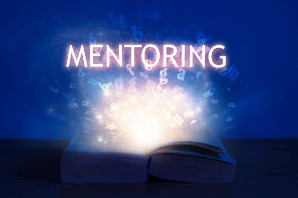 istock Open book with mentoring inscription. Light coming from open book with word mentoring. 1263651606