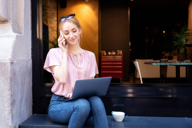 istock Smiling young woman using mobile phone and laptop while sitting in the cafe 1263653027