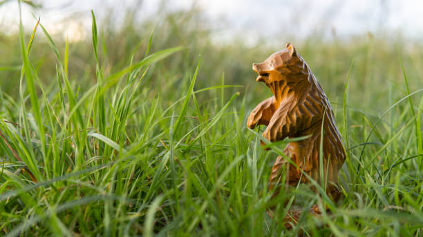 クマの小さな彫刻された姿。木彫り。外の緑の草の中に木製のクマの彫刻が立っています。