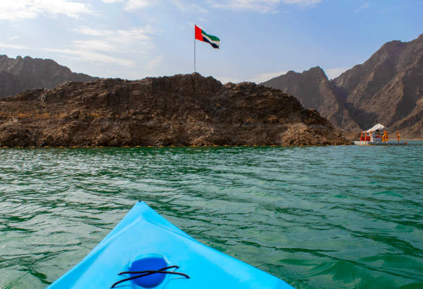 drapeau des émirats arabes unis agitant sur le dessus d’une colline dans le lac de milieu de hatta avec le kayak bleu dans la couleur sur un premier plan - canoe kayak, jaune photos et images de collection