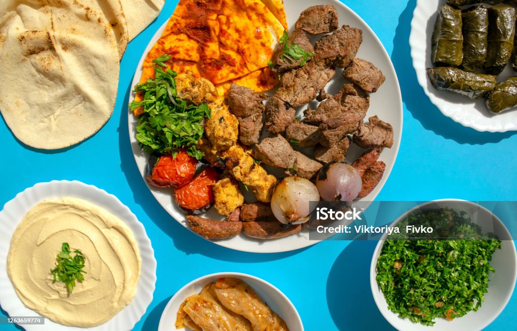 Grilled chicken, lamb, beef, sausages, vegetables, pita bread, tahini sauce, mahshi, stuffed vine leaves, tabbouleh salad on blue background Famous traditional Arabic, Turkish, Israel food. Grilled chicken, lamb, beef, sausages, vegetables, pita bread, tahini sauce, mahshi, stuffed vine leaves, tabbouleh salad on blue background, top view Food Stock Photo