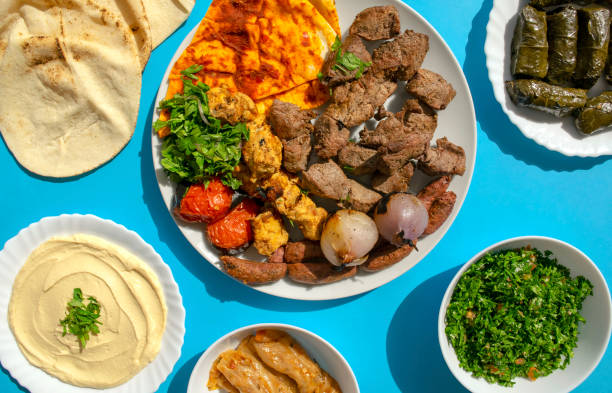 Grilled chicken, lamb, beef, sausages, vegetables, pita bread, tahini sauce, mahshi, stuffed vine leaves, tabbouleh salad on blue background stock photo