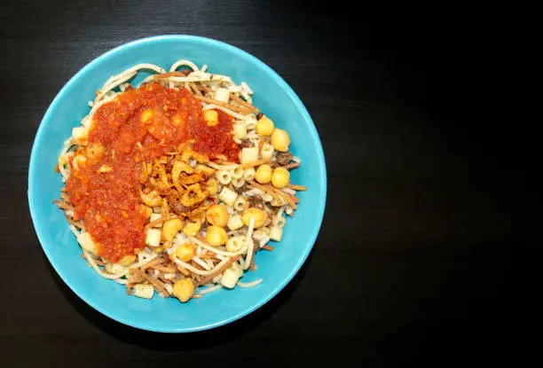 Photo of National Kushari in a turquoise plate on dark wooden background with copy space