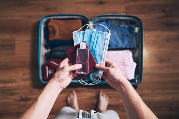 Preparing for travel in new normal Preparing for travel in new normal. Man packing passport, face masks and hand sanitizer. Themes personal protection and flight rules during coronavirus pandemic. new normal concept stock pictures, royalty-free photos & images