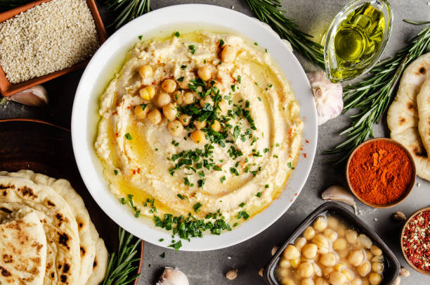 hummus topped with chickpeas, olive oil and green coriander leaves on stone table with pita bread and spices aside. flat lay - aside imagens e fotografias de stock