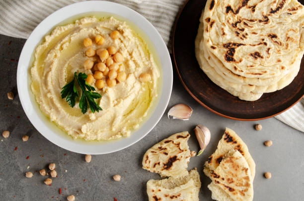 istock Flat lay view at hummus topped with chickpeas and green coriander leaves on stone table served with traditional Pita bread 1263663049