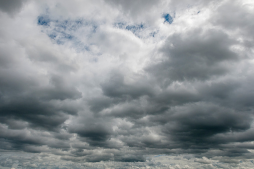 Gloomy and overcast scyscape, many dark storm clouds up to the horizon, little patches of blue sky and white clouds in the foreground. A sky only, full-frame and close-up image