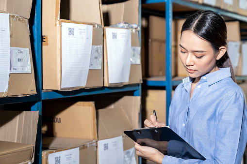 Close up of Asian smart businesswoman working with product inventory in distribution warehouse. For business warehouse inventory and logistic concept.