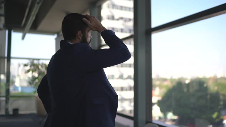 Worried businessman looking through window contemplating on the office