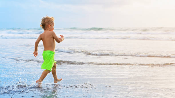 istock Child run with splashes by water pool along sea surf 1263672964