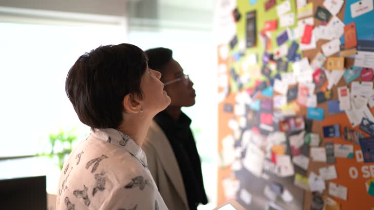 Coworkers planning with digital tablet having new ideas close to bulletin board at work