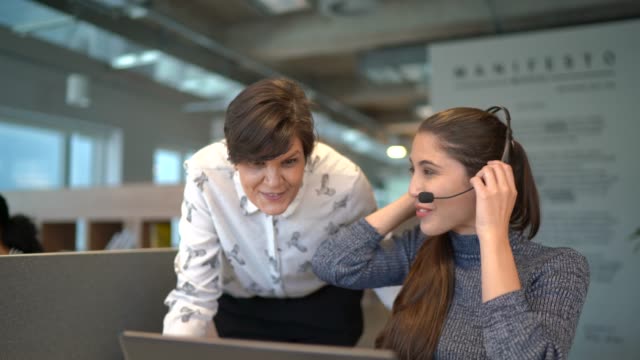 Leader businesswoman helping it support employee with headset at work