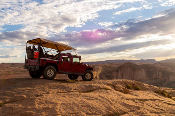 Off Road Vehicle on Sandstone Summit in Hell's Revenge Area Near Moab Utah Overlooking Colorado River July 24, 2020 - Moab, UT, USA: Shown is a customized off road vehicle used to traverse the slickrock trails of southern Utah.  This shot was taken on the Hell's Revenge trail east of Moab. In the distance are the formations in Arches National Park and the Colorado river.  The sun is setting over the river valley in the distance. slickrock trail stock pictures, royalty-free photos & images