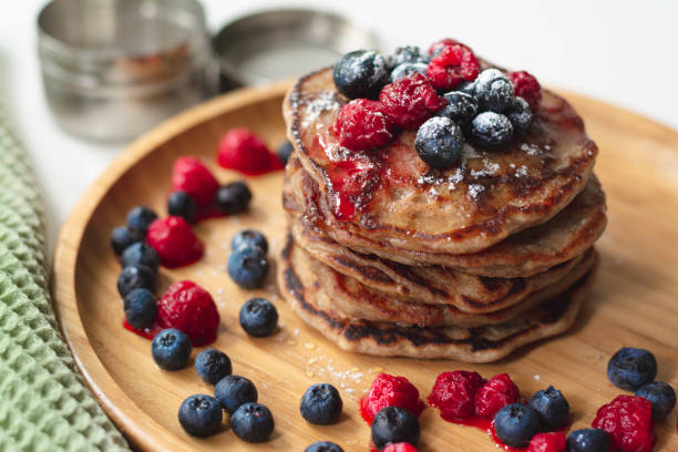 a heap of healthy vegan gluten free whole grain pancakes made with buckwheat flour topped with raspberries and blueberries with icing sugar sprinkled on top - nobody maple tree deciduous tree tree imagens e fotografias de stock