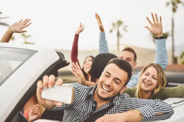 Happy friends taking selfie with mobile smartphone camera in convertible car - Young people having fun in cabriolet auto during road trip vacation - Travel and youth technology lifestyle concept