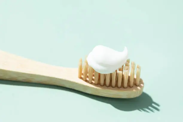 Bamboo toothbrush with toothpaste on mint background. Close up view in sunlight.