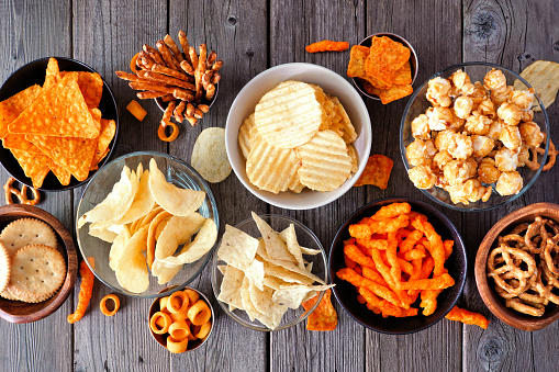 Assortment of salty snacks. Top view table scene on a dark wood background.