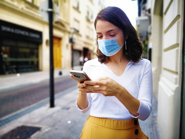 istock Young female texting outdoors wearing a mask for Covid 19 prevention 1263690353
