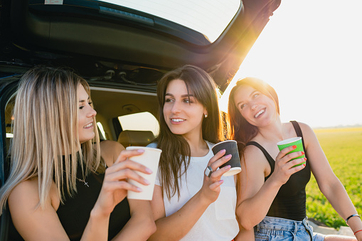 Girls have coffee break at car trunk