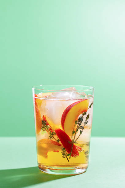 sparkling cold brew peach tea with thyme in glass on green paper background - peach juice imagens e fotografias de stock