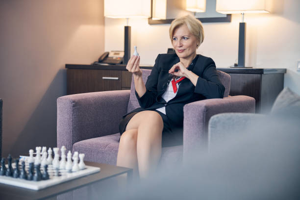 femme d’affaires charmante jouant aux échecs dans la chambre d’hôtel - chess board room business strategy photos et images de collection