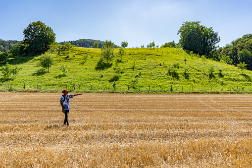 African woman walking on golden harvested corn field in hot summer afternoon. Traveler woman showing far away to the end of the golden field. Near to the famous place Linn at Bözberg in Switzerland.
