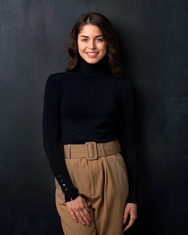 Portrait shot of happy young woman wearing turtleneck sweater while posing at dark background.