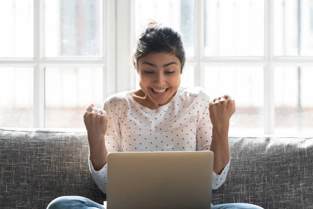 Indian woman in anticipation online lottery result holds fists together hopes for luck Indian woman in anticipation online lottery result holds fists together hopes for luck, girl holding pc on lap feeling excitement got loan opportunity from bank, sale big discount better offer concept unusual win stock pictures, royalty-free photos & images