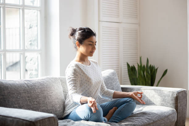istock Indian female sitting on couch lotus pose do yoga exercise 1263705751