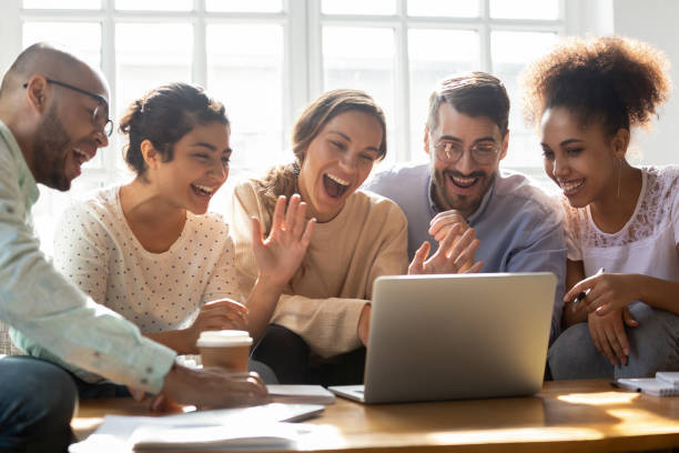 Five multi-ethnic friends make videocall looking at laptop screen Five multi-ethnic millennial friends sitting on sofa looking at computer screen wave hands laughing enjoy distant communication with mate. Make videocall, greeting online by webcam modern tech concept divergent movie review stock pictures, royalty-free photos & images