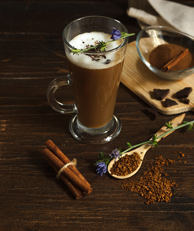 Cappuccino from chicory root, a delicious and healthy drink, a coffee substitute that does not contain caffeine. On a dark wooden table with flowers and granulated chicory