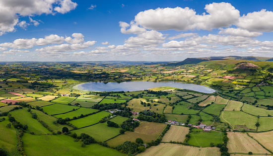 Aerial view of a lake surrounded by green farmland and rolling hills (Llangorse Lake, Wales UK)