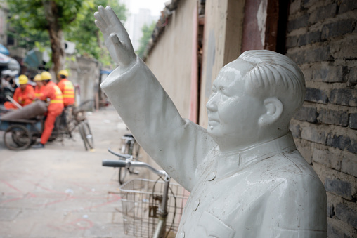 Ceramic Chairman Mao statues and other figurines standing beside a street stall in an antiques market in the Old Town district of Shanghai, China