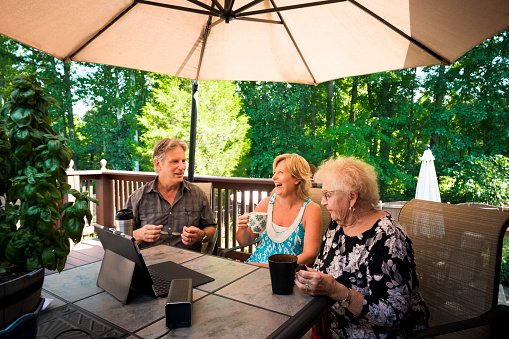 Adult man and wife and senior aged woman interact while watching a program on a digital tablet computer outdoors on the back patio, Indiana, United States