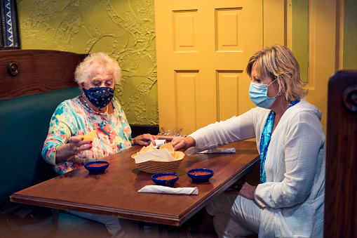 Two women wearing face masks prepare to eat tortilla chips, Indiana, USA