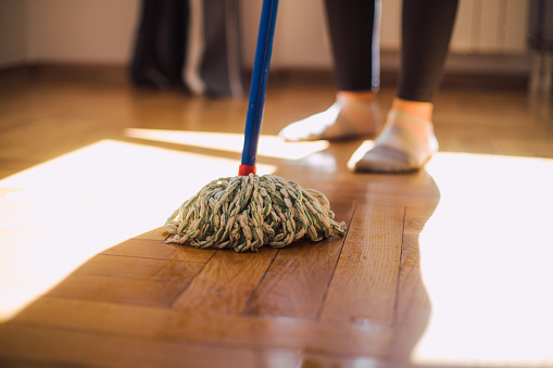 Closeup view of a mop cleaning the floor. Someone's feet are visible in the background.