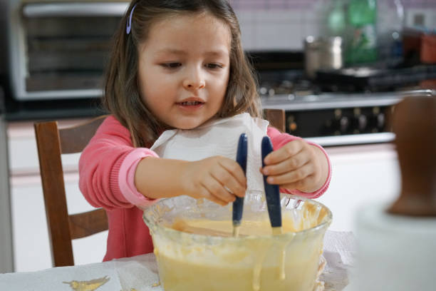istock Beautiful little girl playing with spoon and dough while cooking during quarantine 1263734452