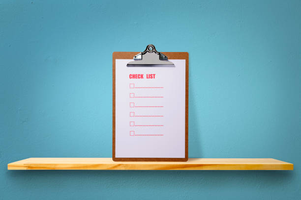 Standing clipboard with checklist on a wooden shelf against blue wall with copy space.