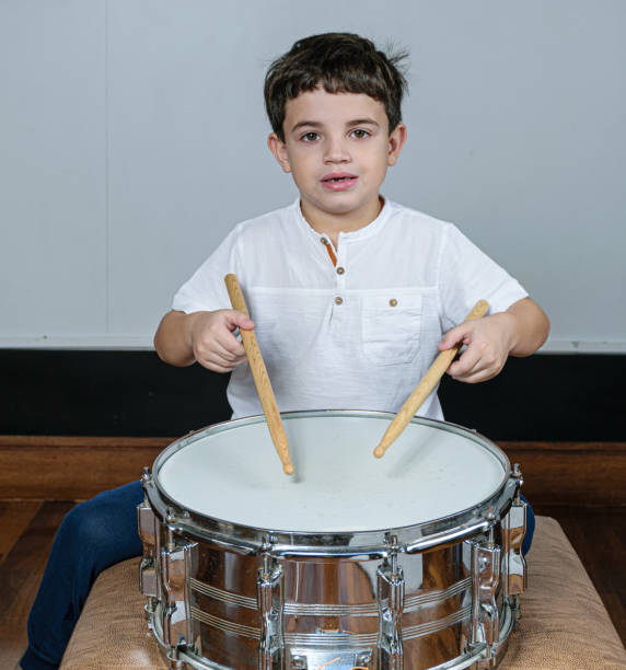 istock 7 year old child staring at the camera and playing the drums. 1263738441