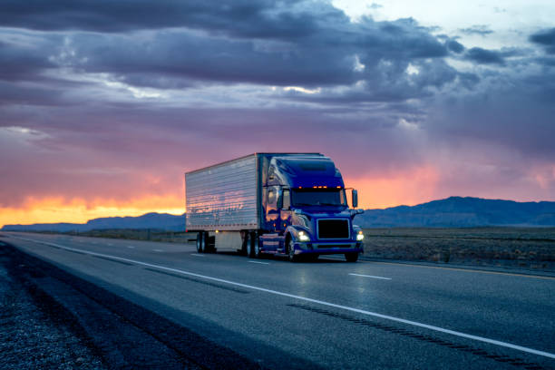 heavy hauler semi-trailer tractor truck speeding down a four-lane highway with a dramatic and colorful sunset or sunrise in the background - four lane highway stock-fotos und bilder
