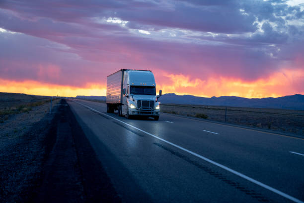 abendaufnahme eines sattelschleppers (weiß), der vor einem atemberaubenden, bunten wolkenverhangenen sonnenuntergang oder sonnenaufgang auf einem vierspurigen desert interstate highway unterwegs ist - multidirectional stock-fotos und bilder