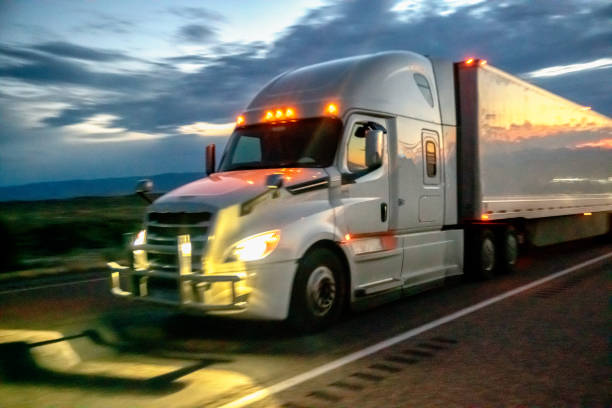 close image eines weißen sattelzug-traktors mit scheinwerfern und lauflichtern beleuchtet auf einem vierspurigen highway in der dämmerung - four lane highway stock-fotos und bilder