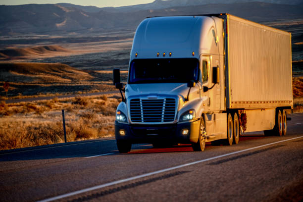 istock Evening Sunlight on a Large White Semi-Trailer Tractor Truck as the Driver Goes down a Four-Lane Highway in a Desert 1263741309