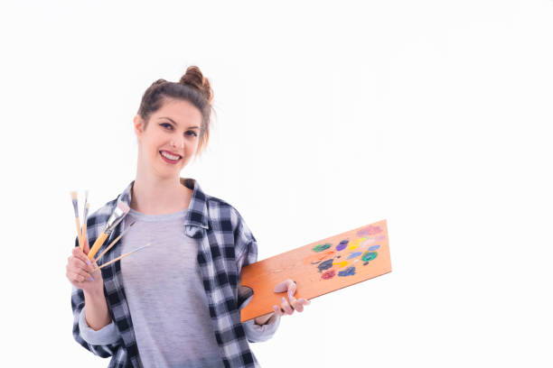 Beautiful young woman holding a painter palette and an assortment of paintbrushes on a light background. Artistic concept.