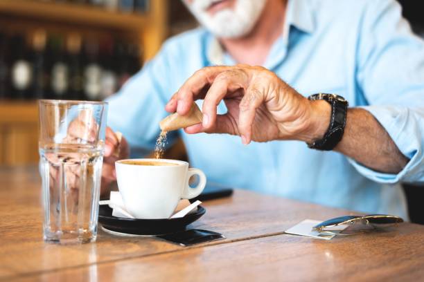 senior mann gießt zucker in kaffee im restaurant - sugar sachet stock-fotos und bilder